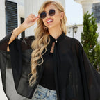 Femme blonde portant cape poncho noir col montant avec bouton perle, lunettes de soleil