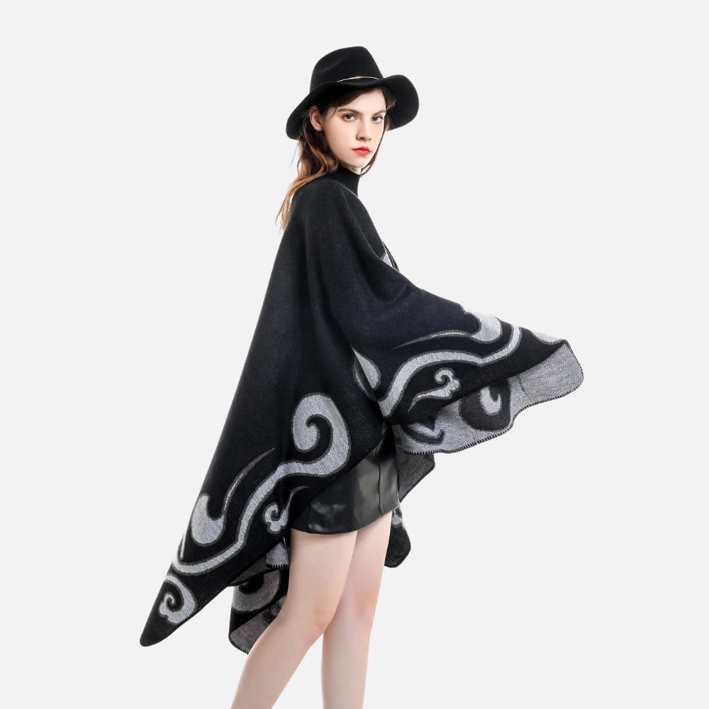 Femme portant cape poncho noire réversible avec motif arabesques gris, vue de dos, chapeau noir