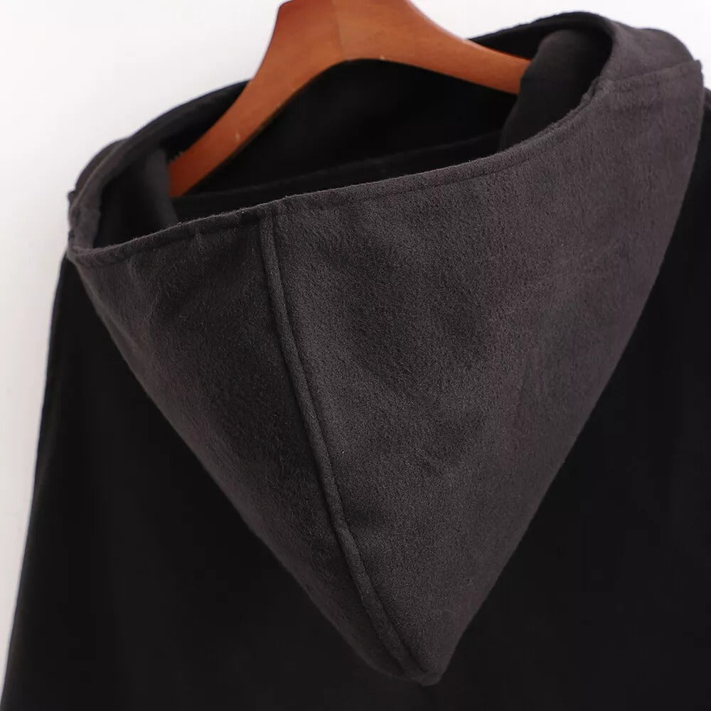 Cape poncho noire longue avec capuche intégrée, vue de dos sur cintre en bois