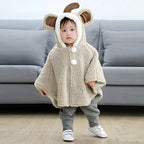 Bébé portant cape poncho polaire beige avec capuche oreilles et pompons blancs