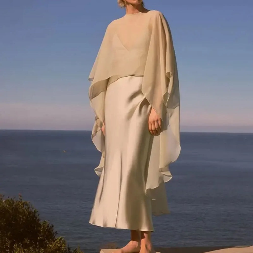 Femme portant cape poncho voile beige transparent sur plage avec vue mer en arrière-plan