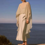 Femme portant cape poncho voile beige transparent sur plage avec vue mer en arrière-plan