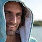 Homme souriant portant un poncho de bain microfibre bicolore vert et bleu avec capuche et manches courtes
