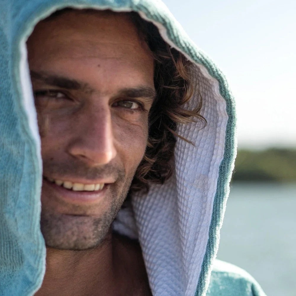 Homme souriant portant un poncho de bain microfibre bicolore vert et bleu avec capuche et manches courtes
