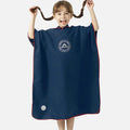 Enfant souriant portant un poncho de bain microfibre bleu marine avec capuche et logo VOCOOL