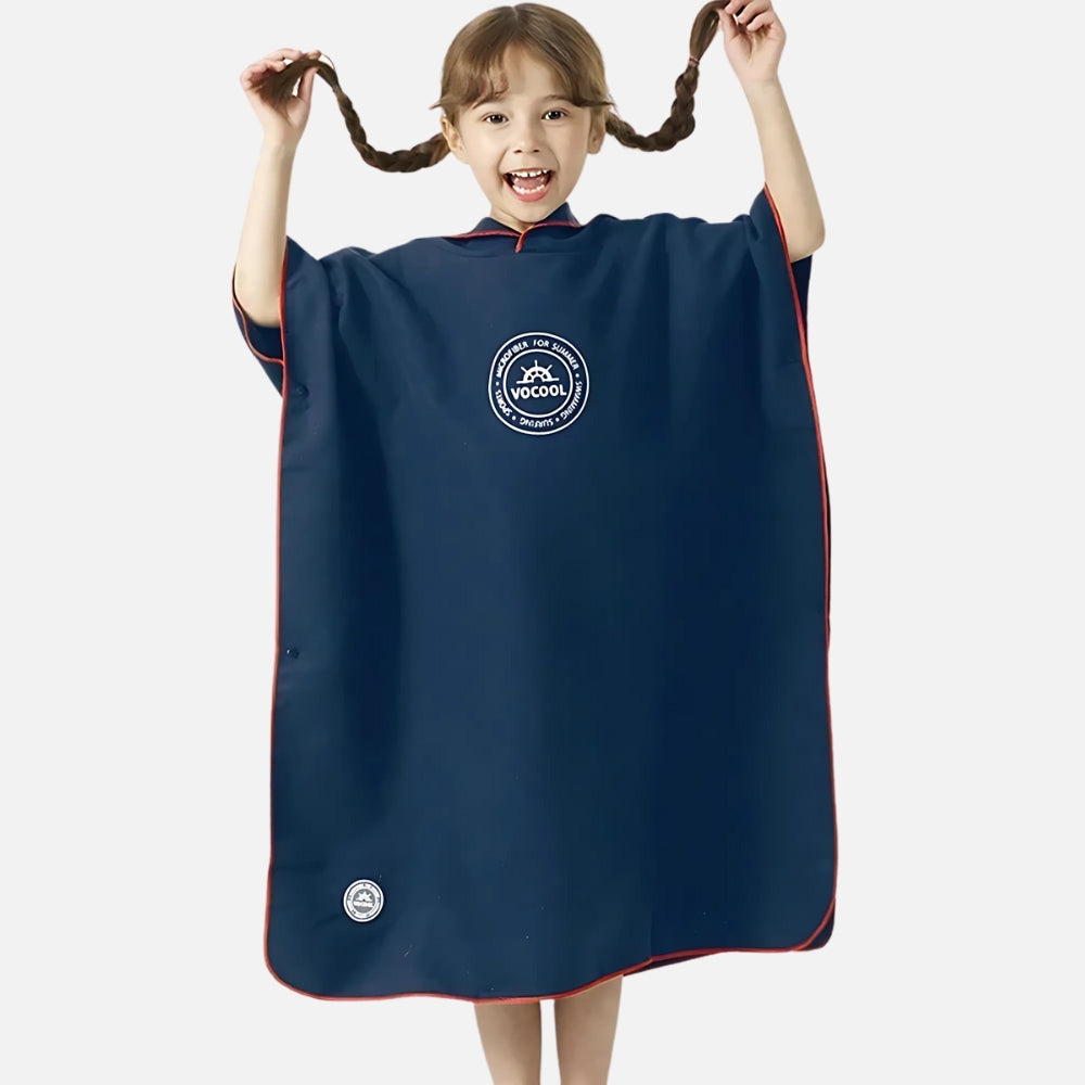 Enfant souriant portant un poncho de bain microfibre bleu marine avec capuche et logo VOCOOL