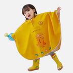 Enfant souriant portant un poncho de pluie jaune avec dinosaure et capuche