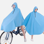 Deux femmes portent un poncho pluie bleu avec capuche et visière, l'une à vélo