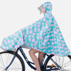 Femme à vélo portant poncho pluie turquoise fleurs roses avec capuche et visière