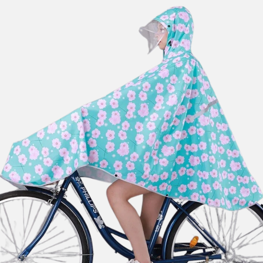 Femme à vélo portant poncho pluie turquoise fleurs roses avec capuche et visière