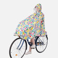Femme à vélo portant poncho pluie coloré motifs géométriques avec capuche et visière