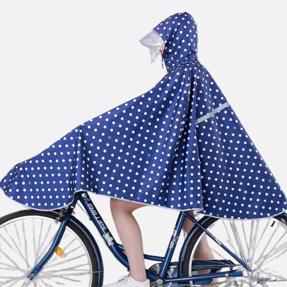 Femme à vélo portant un poncho de pluie bleu marine à pois blancs avec capuche et visière