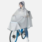 Femme à vélo portant un poncho pluie transparent gris avec capuche et visière réfléchissante