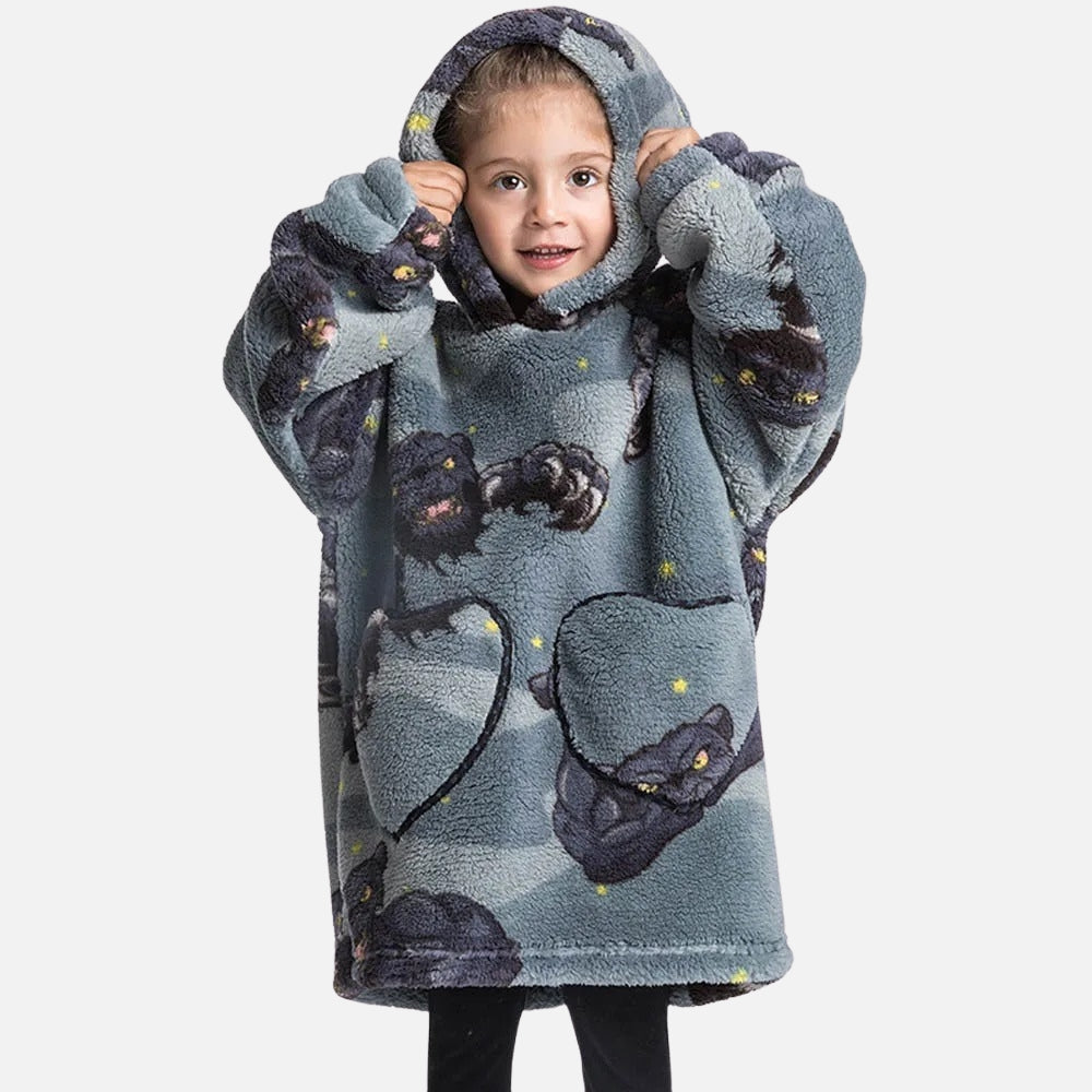 Enfant souriante portant un poncho polaire gris à capuche avec panthères noires et étoiles