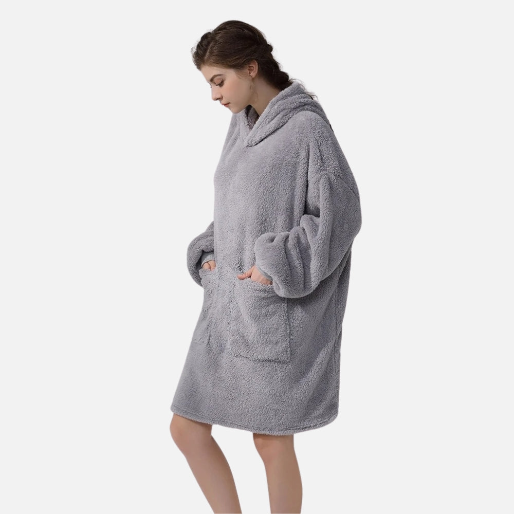 Femme portant un poncho polaire gris avec capuche et manches longues, mains dans les poches
