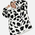 Femme souriante portant poncho polaire sherpa noir et blanc motif vache avec capuche