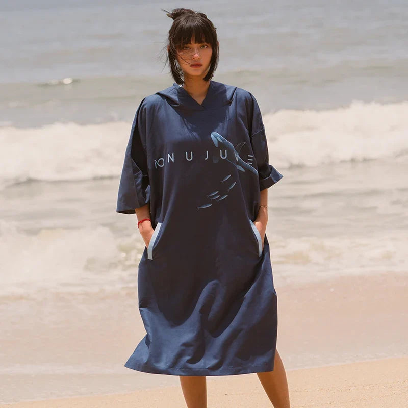 Femme portant poncho surf microfibre bleu marine avec capuche sur plage, vue de face
