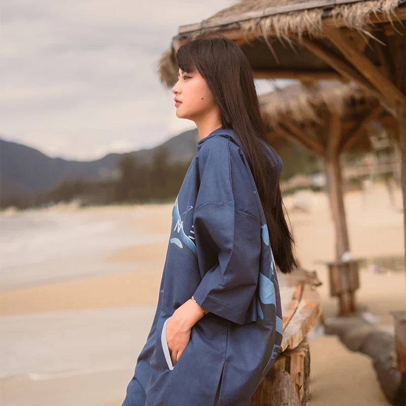 Femme de dos portant un poncho surf microfibre bleu marine à capuche près d'une plage