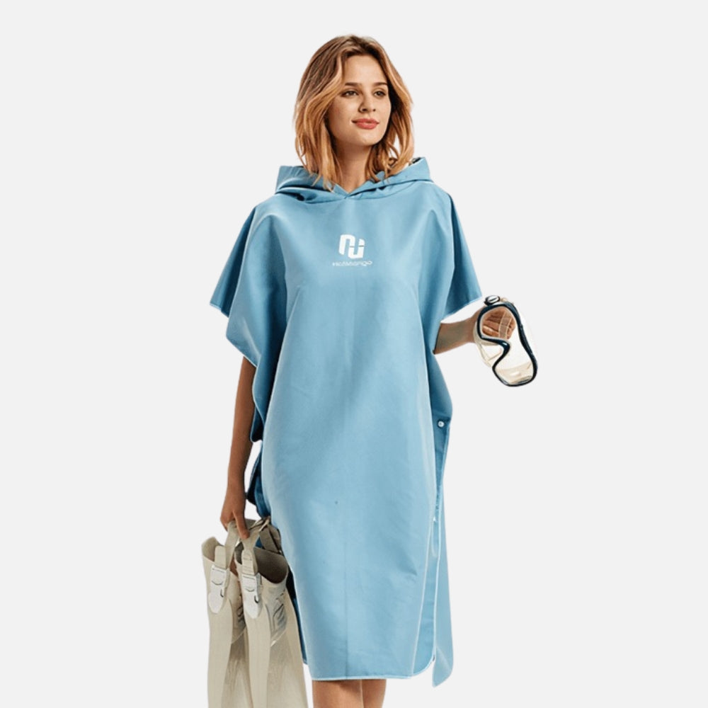 Femme portant poncho surf microfibre bleu avec capuche et logo, tenant accessoires plage