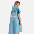 Femme portant poncho surf microfibre bleu capuche, logo surfing dos, séchage rapide