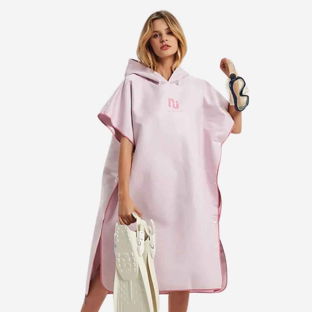 Femme portant un poncho surf rose microfibre à capuche avec logo, tenant accessoires de plage